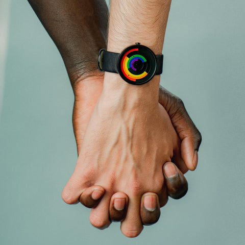 Pride watch worn by one of two men holding hands on light blue background